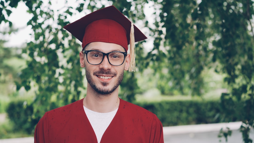 A smiling graduate in a red cap and gown outdoors.